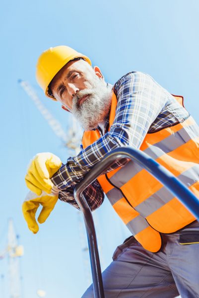 Bearded construction worker in reflective vest and hardhat leaning on guardrail