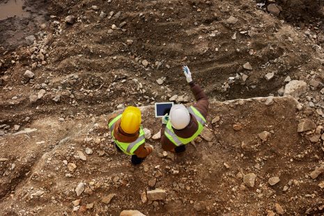 Above view shot of two industrial  workers wearing reflective jackets standing on mining worksite outdoors using digital tablet, copy space